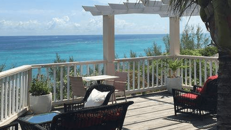 White wood terrace overlooking the Caribbean sea with several lounge chairs and dining chairs at Stone's Throw Away Inn in Nassau Bahamas